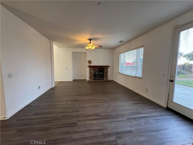 unfurnished living room featuring dark wood-type flooring, ceiling fan, and a brick fireplace