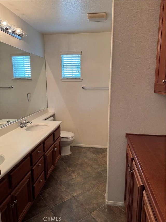 bathroom with a healthy amount of sunlight, toilet, vanity, and a textured ceiling