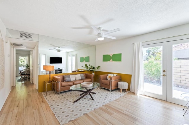 living room featuring ceiling fan, french doors, a textured ceiling, and light hardwood / wood-style floors