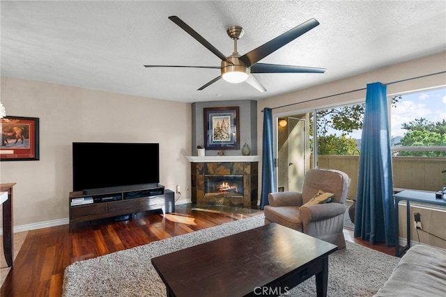 living room with a textured ceiling, ceiling fan, a fireplace, and dark hardwood / wood-style flooring