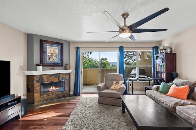 living room with ceiling fan, a textured ceiling, dark hardwood / wood-style flooring, and a tile fireplace