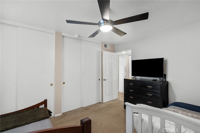 carpeted bedroom with ceiling fan, multiple closets, and a textured ceiling