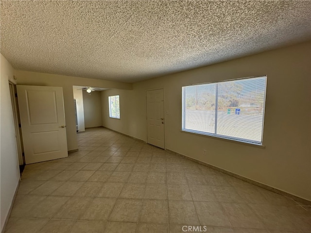 spare room with a textured ceiling, light tile patterned flooring, and ceiling fan