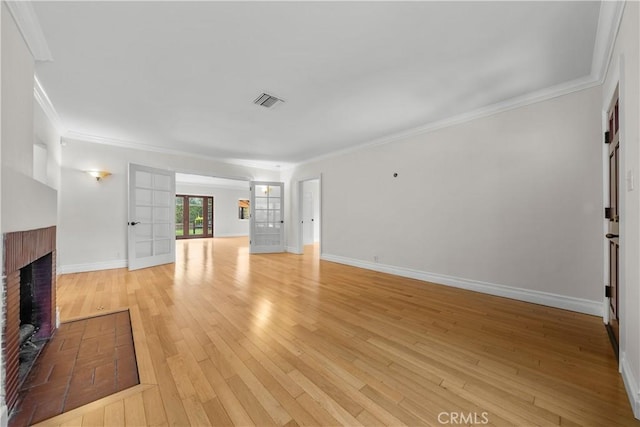 unfurnished living room with crown molding, french doors, light wood-type flooring, and a brick fireplace