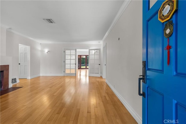 entrance foyer featuring a fireplace, light hardwood / wood-style floors, crown molding, and french doors