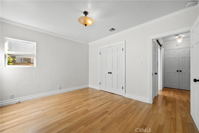 unfurnished bedroom featuring a barn door, light hardwood / wood-style floors, and ornamental molding