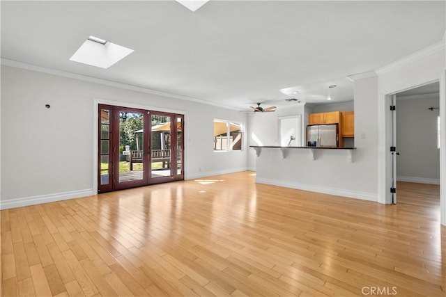 unfurnished living room featuring a skylight, crown molding, ceiling fan, and light wood-type flooring