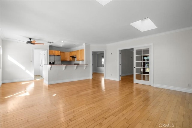 unfurnished living room with light hardwood / wood-style floors, a skylight, ornamental molding, and ceiling fan