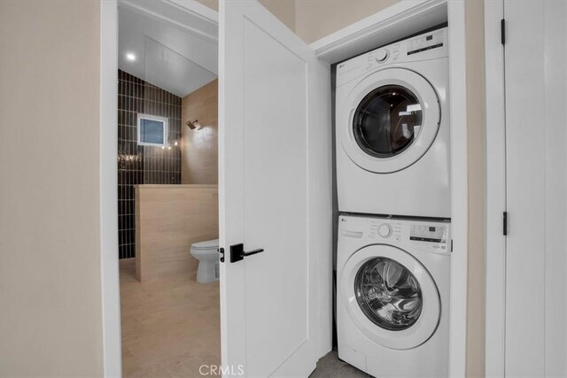 clothes washing area with stacked washer and clothes dryer and tile walls