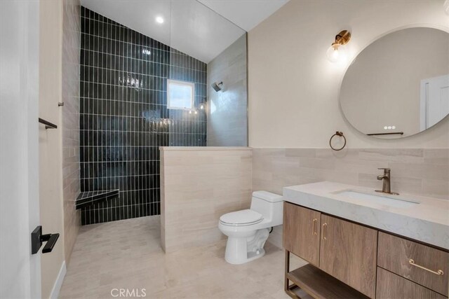 bathroom featuring tile walls, tile patterned flooring, vanity, a tile shower, and toilet