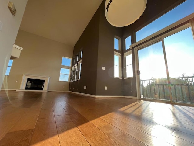 unfurnished living room with wood-type flooring, a healthy amount of sunlight, and a high ceiling