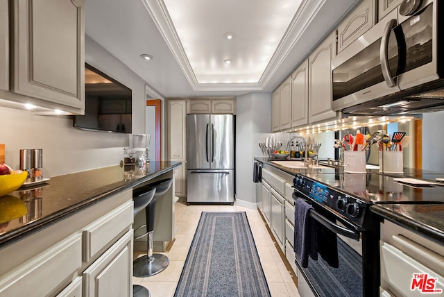 kitchen featuring sink, light tile patterned floors, dark stone counters, a raised ceiling, and stainless steel appliances