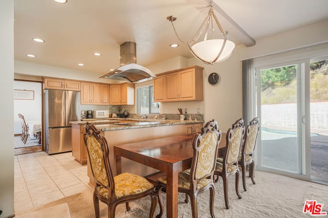 kitchen featuring light brown cabinets, dark stone countertops, decorative light fixtures, island range hood, and stainless steel refrigerator