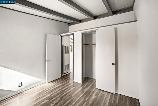 unfurnished bedroom with a closet, hardwood / wood-style flooring, and beamed ceiling