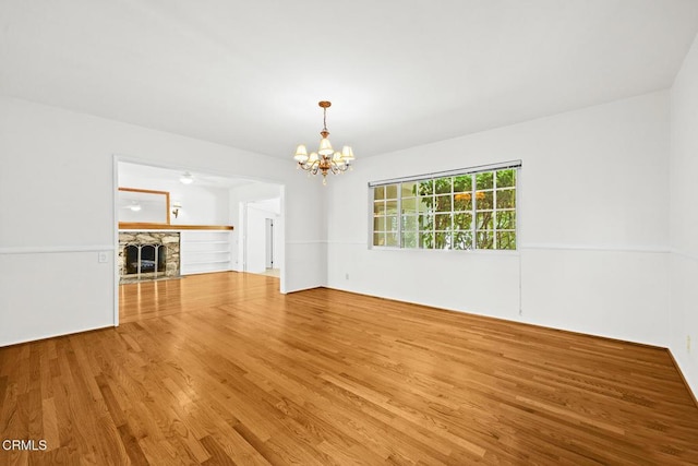 unfurnished living room with a chandelier, hardwood / wood-style floors, and a stone fireplace