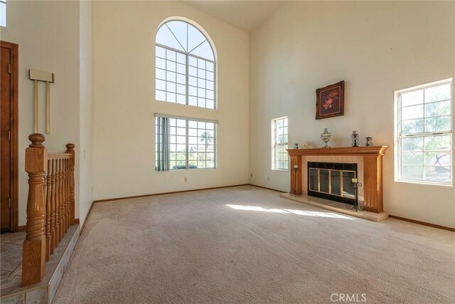 unfurnished living room with plenty of natural light, light colored carpet, and a high ceiling