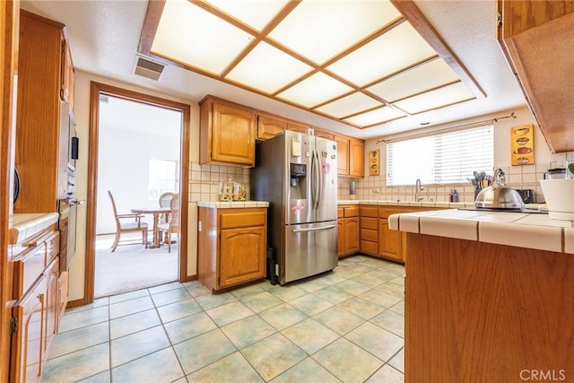 kitchen with stainless steel refrigerator with ice dispenser, tile countertops, and tasteful backsplash