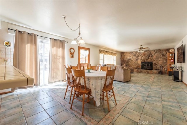 tiled dining room with a fireplace and ceiling fan with notable chandelier