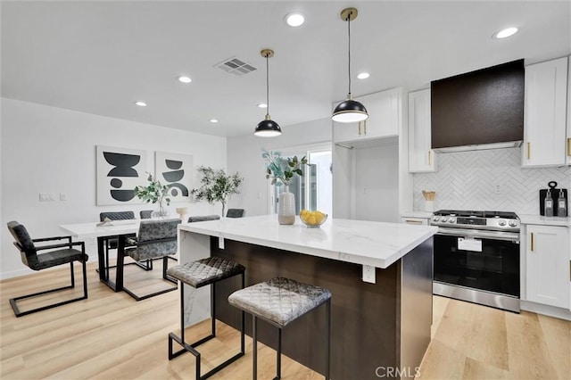 kitchen featuring white cabinets, hanging light fixtures, light wood-type flooring, stainless steel range, and a kitchen island