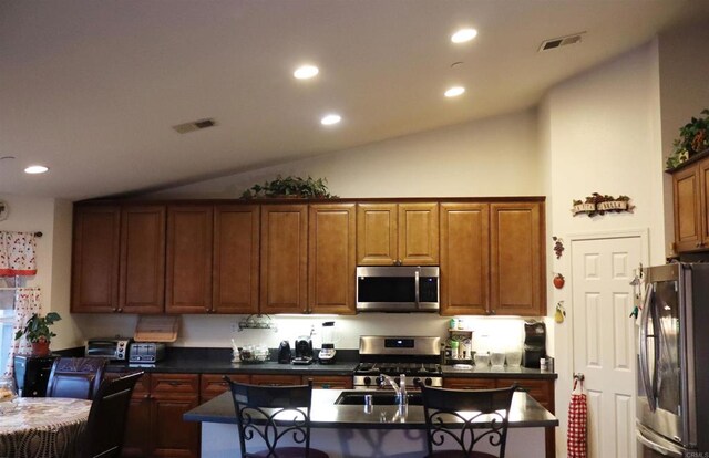 kitchen with sink, stainless steel appliances, an island with sink, and vaulted ceiling