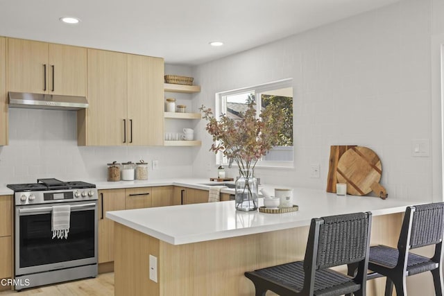 kitchen featuring light brown cabinets, light hardwood / wood-style flooring, kitchen peninsula, gas range, and a breakfast bar