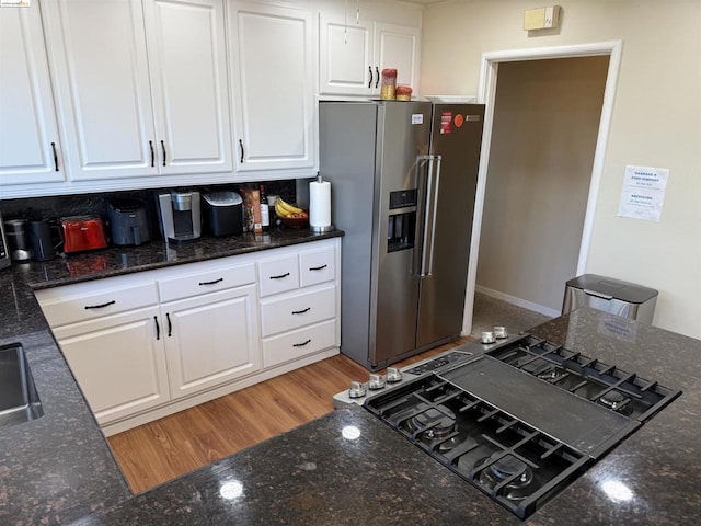 kitchen featuring white cabinets, black stovetop, stainless steel fridge with ice dispenser, dark stone countertops, and wood-type flooring