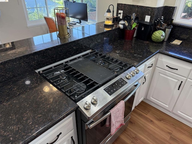 kitchen featuring high end stove, dark stone countertops, white cabinetry, and hardwood / wood-style flooring