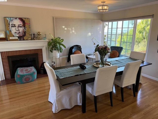 dining area with light wood-type flooring, crown molding, and a brick fireplace