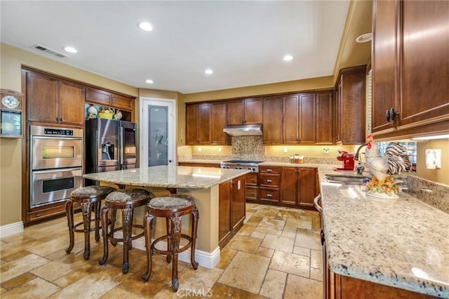 kitchen with a kitchen island, light stone countertops, sink, and appliances with stainless steel finishes