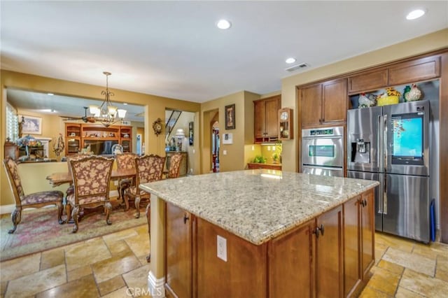 kitchen featuring a center island, an inviting chandelier, light stone counters, pendant lighting, and appliances with stainless steel finishes