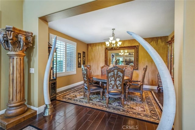 dining area featuring dark wood-type flooring, wooden walls, and an inviting chandelier