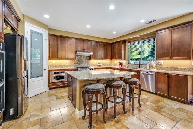 kitchen with sink, appliances with stainless steel finishes, a kitchen island, light stone counters, and a breakfast bar area