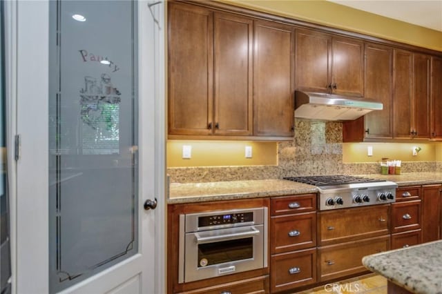 kitchen featuring backsplash, light stone counters, and stainless steel appliances