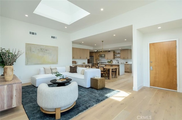 living room with light wood-type flooring, a skylight, and sink