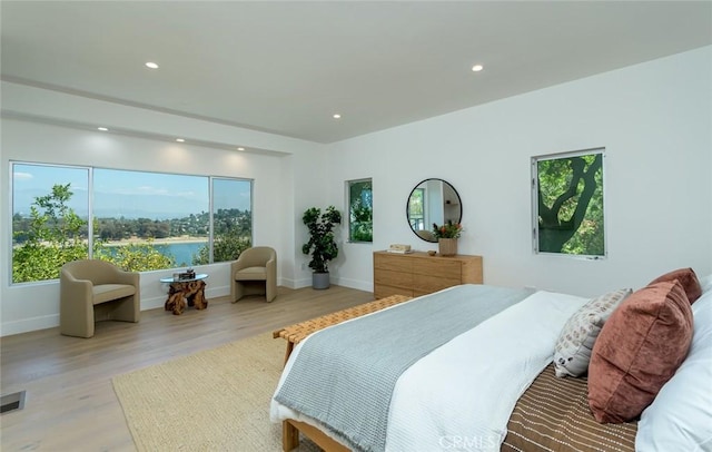 bedroom featuring multiple windows, a water view, and light wood-type flooring