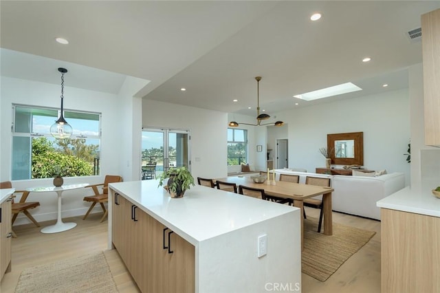 kitchen featuring a skylight, light wood-type flooring, light brown cabinetry, decorative light fixtures, and a kitchen island