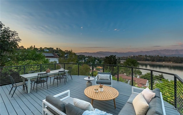 deck at dusk with outdoor lounge area and a water and mountain view