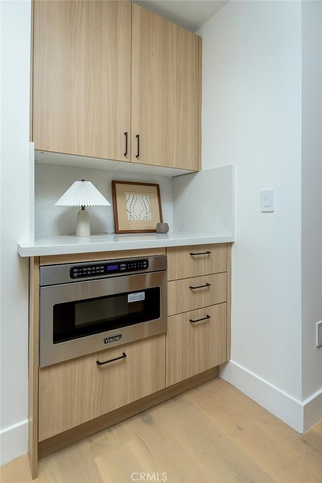 kitchen with light brown cabinets, oven, and light hardwood / wood-style flooring