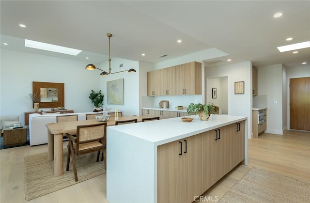 kitchen featuring light brown cabinets, light wood-type flooring, a skylight, and decorative light fixtures