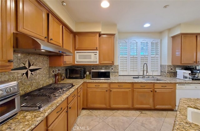 kitchen with appliances with stainless steel finishes, backsplash, a sink, and under cabinet range hood