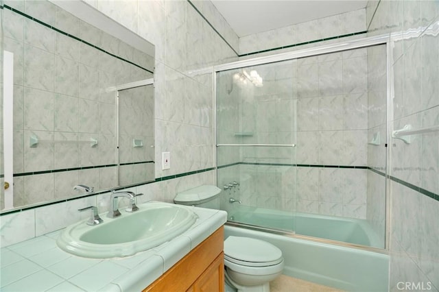 full bathroom featuring toilet, tile walls, vanity, and bath / shower combo with glass door