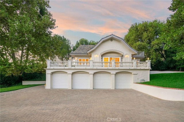 view of front of property featuring decorative driveway, a balcony, a garage, and stucco siding