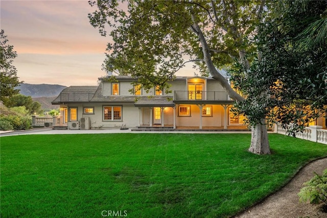 back of house featuring a patio, a balcony, stucco siding, a lawn, and a mountain view