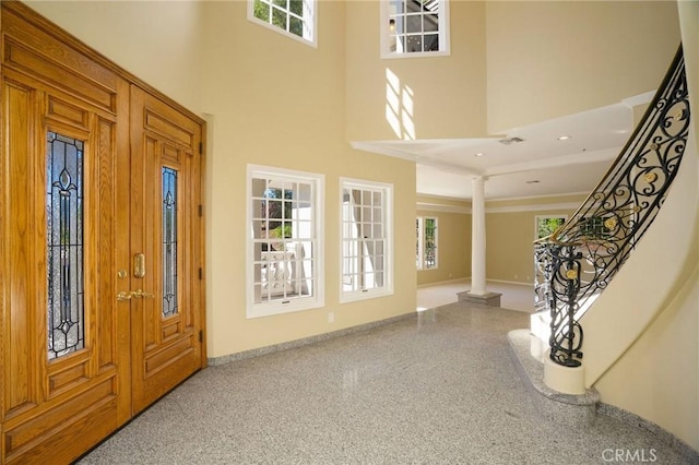 foyer entrance with visible vents, decorative columns, stairway, a high ceiling, and speckled floor