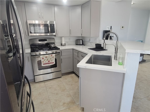 kitchen with kitchen peninsula, light tile patterned floors, appliances with stainless steel finishes, gray cabinetry, and sink