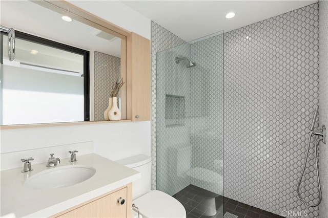 bathroom with a tile shower, vanity, and toilet