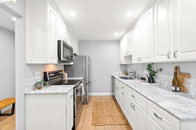 kitchen with stainless steel appliances, white cabinets, light hardwood / wood-style flooring, light stone counters, and sink