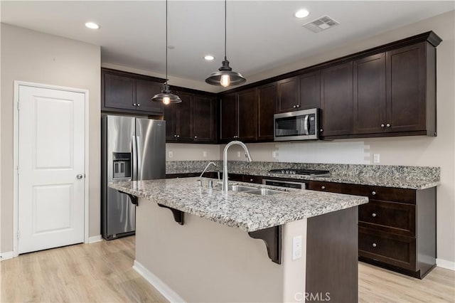 kitchen with pendant lighting, a kitchen island with sink, sink, light wood-type flooring, and stainless steel appliances