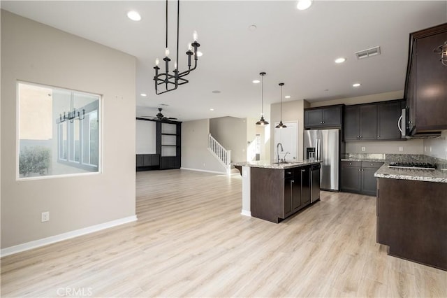 kitchen featuring appliances with stainless steel finishes, ceiling fan with notable chandelier, sink, decorative light fixtures, and an island with sink