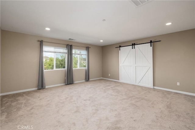 spare room with a barn door and light colored carpet